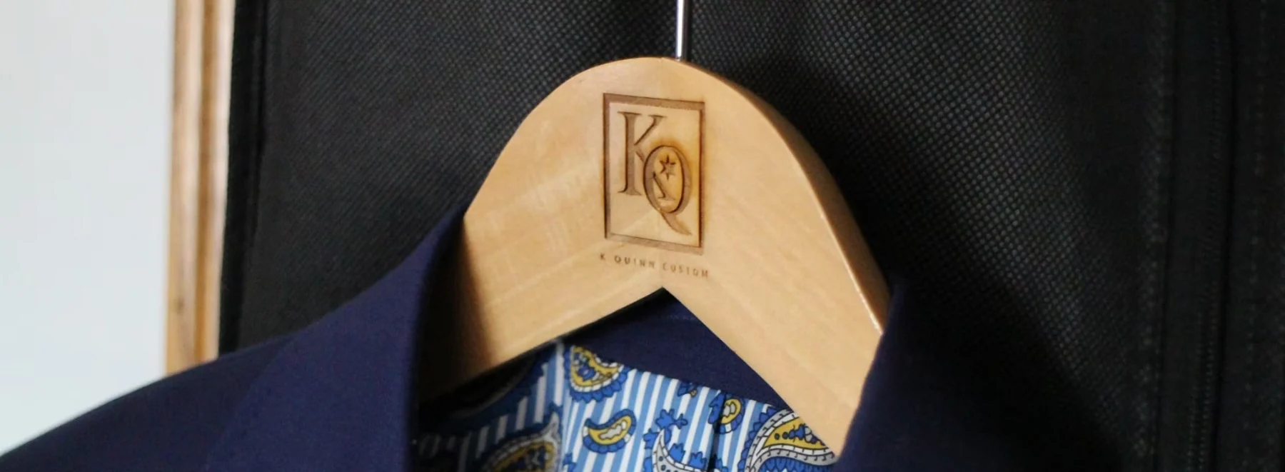 Approved wooden KQuinn hanger with its engraved logo and navy garment